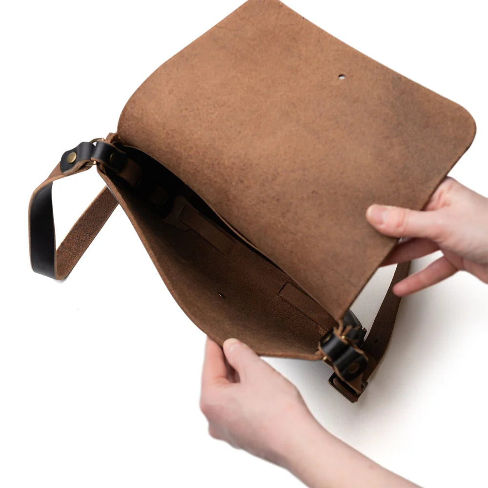 Brown leather bag held open by a hand on a white background