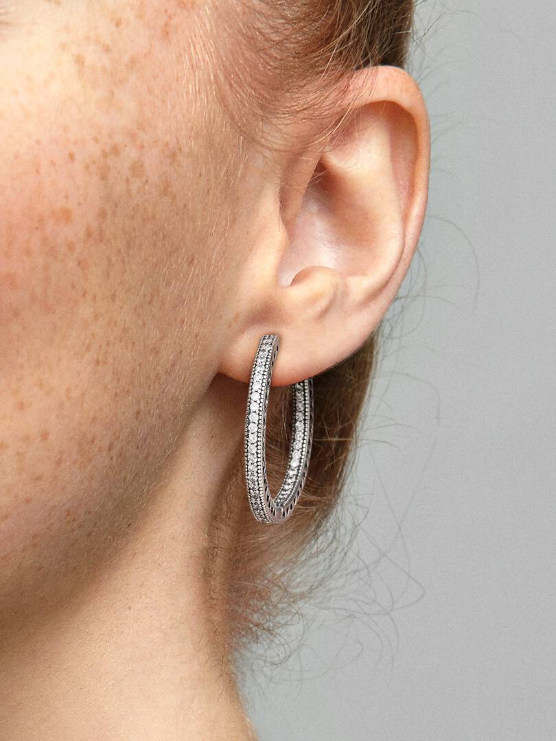 Silver hoop earrings worn by a person with a neutral background