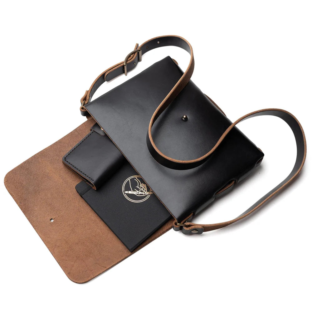 Black leather bag opened with a notebook and phone inside.