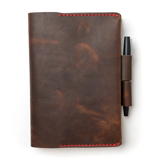 Brown leather notebook with red stitching and a pen on a white background